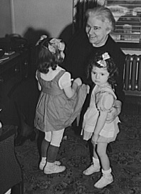 Black and white photograph shows Sister Kenny crouching down to talk to two children.